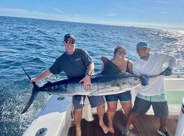Three smiling people on a sportfishing boat holding a huge billfish over the deck on a sunny offshore deep-sea fishing trip.