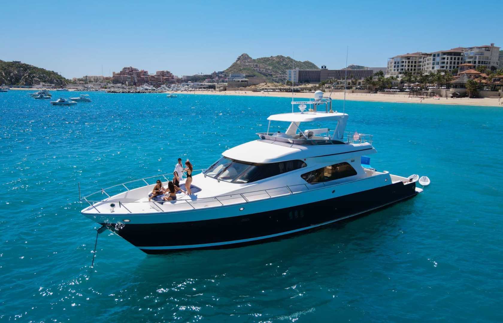 Luxury white motor yacht anchored in clear turquoise water off a sandy beachfront resort on a sunny day, group of people relaxing on the bow — vacation vibe.