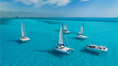 Aerial shot of white catamarans and a powerboat floating in crystal-clear turquoise tropical water under a bright blue sky