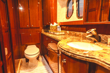 Luxurious yacht bathroom with warm glossy wood paneling, marble vanity and sink, porthole window, and compact toilet