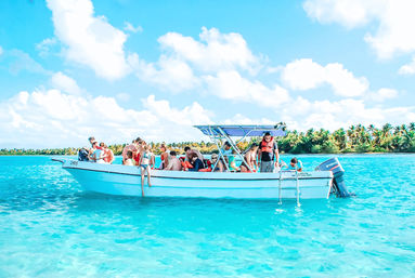 Motorboat with passengers wearing life jackets floating on bright turquoise tropical water near a palm‑lined island under a sunny blue sky