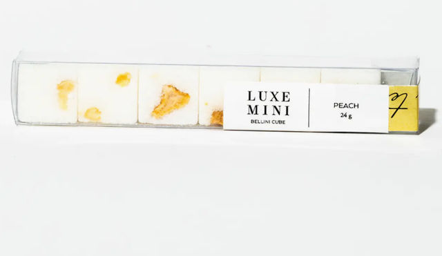 Clear rectangular box of five white mini peach-flavored candy cubes with visible peach pieces and a Peach 24 g label — clean studio product shot on white background.