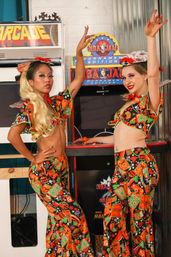 Two performers in matching vibrant casino-print costumes strike poses beside a retro arcade basketball cabinet in an indoor vintage-style arcade.