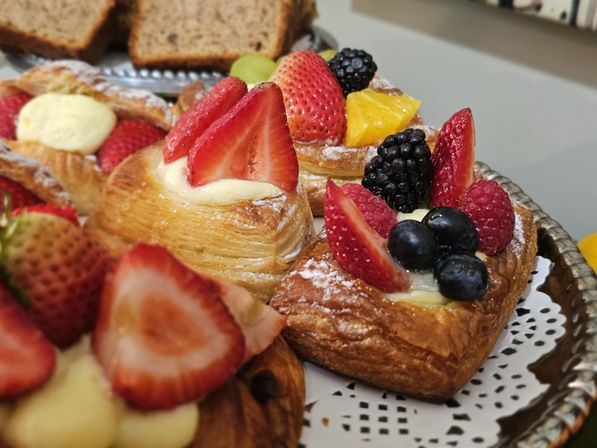 Assorted fruit Danish pastries on a silver platter topped with strawberries, blueberries, blackberries, raspberries and orange segments over vanilla custard — bakery-style brunch display.