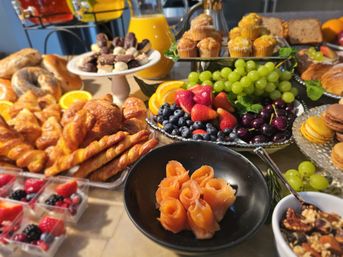Brunch buffet spread with golden croissants and twisted pastries, muffins and macarons, fresh berries, grapes and orange slices, cherries, and smoked salmon rosettes beside pitchers of orange juice.
