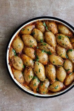Overhead shot of a round pan of golden-brown oven-baked stuffed onions filled with rice and tomato, sprinkled with chopped parsley on a rustic countertop