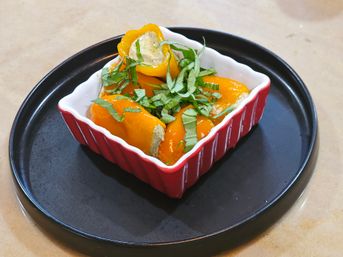 Bright stuffed mini yellow peppers filled with herbed soft cheese and shredded basil, served in a red ramekin on a black serving plate — vibrant appetizer