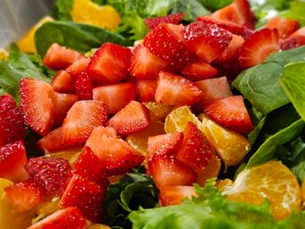 Close-up of a vibrant strawberry and mandarin orange salad with diced strawberries and tangerine segments layered on fresh spinach and mixed greens.