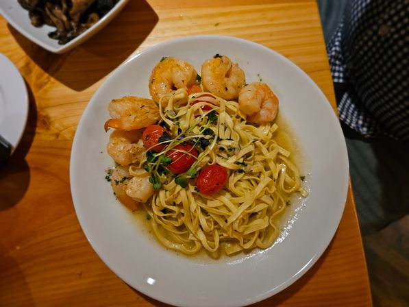Shrimp linguine pasta in garlic-butter sauce with cherry tomatoes and microgreens on a white plate atop a wooden table