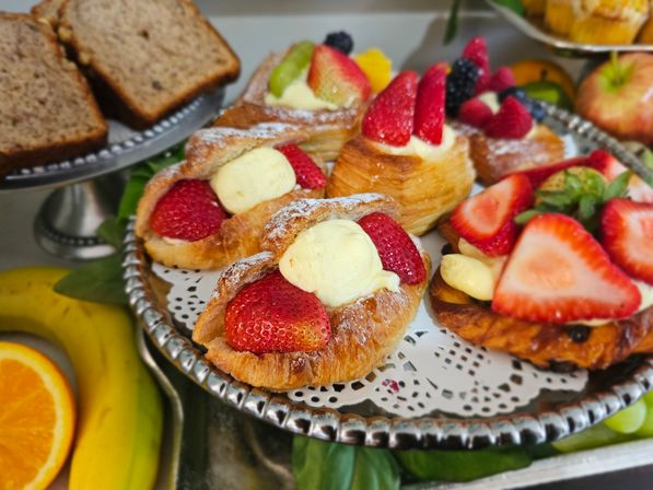 Strawberry cream-filled croissant pastries on a silver serving tray with fresh fruit (banana, orange) and sliced bread — breakfast brunch pastry display