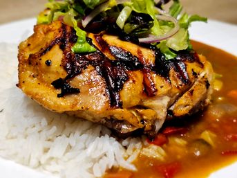 Juicy grilled chicken thigh with charred grill marks on steamed white rice, served with savory brown vegetable sauce and topped with shredded lettuce and red onion — close-up plate shot