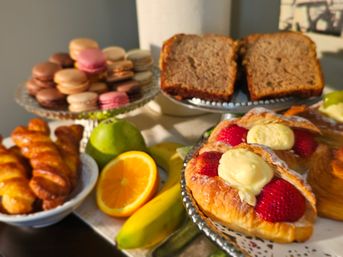 Brunch dessert table with strawberry-custard danishes, assorted macarons, braided pastries, slices of banana bread and fresh orange, banana and pear
