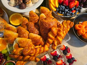 Golden flaky croissants and twisted pastries in a bakery-style brunch spread with fresh blueberries, strawberries, orange slices, smoked-salmon rosettes, mini berry parfaits and assorted chocolates.