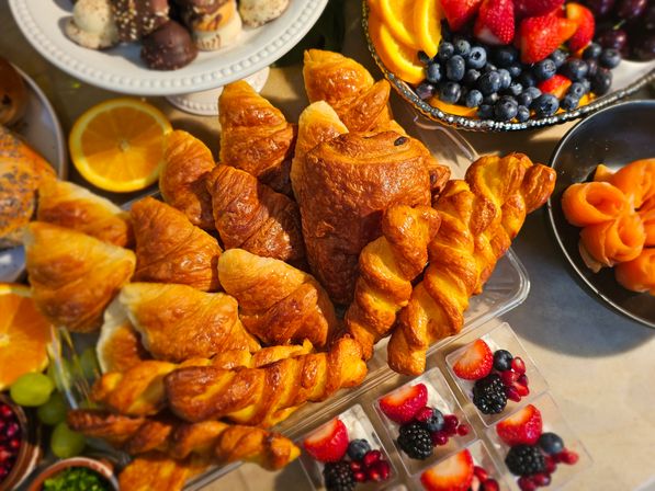 Golden flaky croissants and twisted pastries in a bakery-style brunch spread with fresh blueberries, strawberries, orange slices, smoked-salmon rosettes, mini berry parfaits and assorted chocolates.