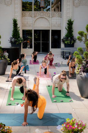 Sunlit outdoor yoga class on colorful mats in an urban courtyard, participants in balancing poses near an ornate building facade and large potted plants