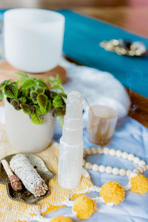 Boho home meditation altar with selenite tower, white sage smudge stick, palo santo, potted plant and wooden bead garland on a blue blanket with yellow pom-poms