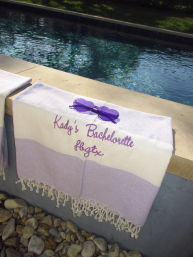 Poolside: purple-striped personalized bachelorette towel draped over the ledge with heart-shaped purple sunglasses and sparkling blue pool water