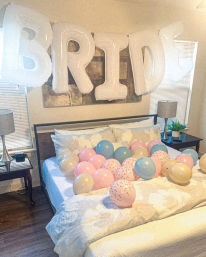 Cozy bedroom decked out for a bride-to-be with giant white letter balloons spelling BRIDE above the bed and pastel pink, blue, and gold balloons scattered across a white comforter.