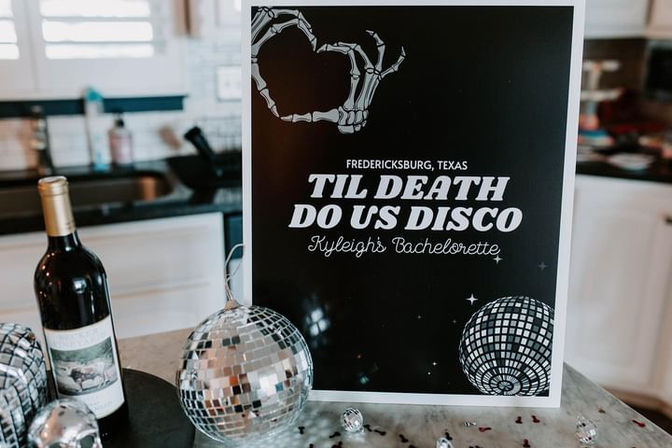 Bachelorette party poster on a kitchen counter in Fredericksburg, Texas that reads Til Death Do Us Disco with a skeletal hand heart graphic, mirrored disco balls, scattered confetti, and a bottle of red wine.