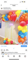 Indoor rainbow balloon arch and column with silver star mylar balloons framing an iridescent fringe curtain and pink neon "love" sign, colorful balloons scattered on a wood floor — festive party photo backdrop.