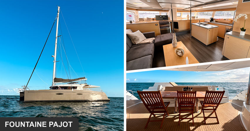 Sunlit catamaran yacht on open blue ocean under a clear sky; bright wood‑finished salon and galley, plus an aft teak dining deck with wooden chairs facing the sea.