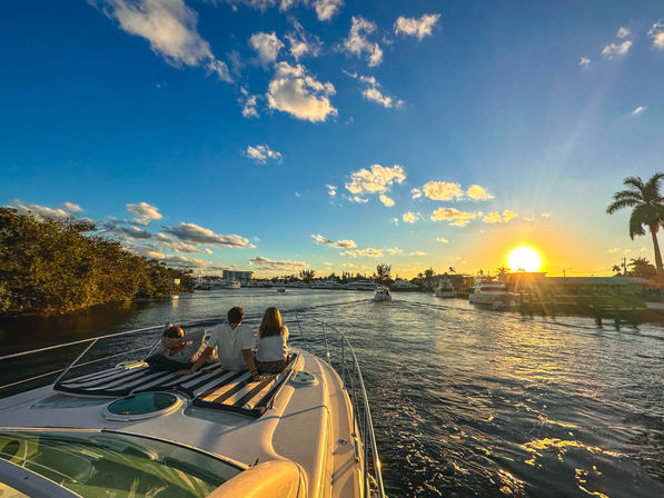 Golden sunset yacht ride through a palm-lined coastal marina with three people relaxing on the bow