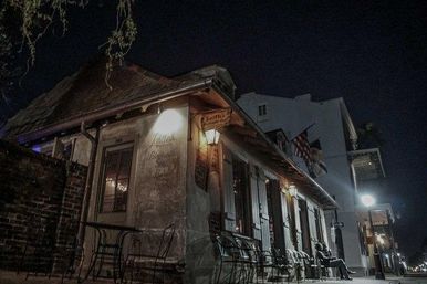 Historic brick corner restaurant with outdoor bistro seating, shuttered windows and warm lanterns on a dimly lit downtown street at night
