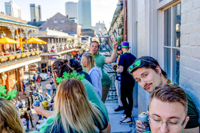Group of people in green on a New Orleans French Quarter balcony watching a lively street celebration, wearing shamrock accessories and holding drinks