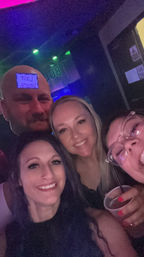 Nightclub selfie of four friends smiling under neon lights, holding drinks and laughing — fun night out vibe