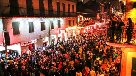 Nighttime New Orleans street packed with a dense party crowd, lit brick buildings and wrought-iron balconies