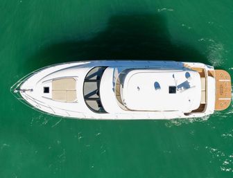 Aerial top-down drone view of a sleek white luxury yacht gliding on emerald green water, showing teak swim platform, foredeck sun pad, and curved windshield