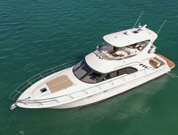 Aerial view of a sleek white luxury motor yacht with flybridge, aft seating and bow sunpad cruising on calm turquoise sea