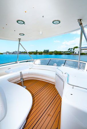 Luxury yacht deck with curved white seating and teak-style flooring overlooking turquoise marina and palm-lined shoreline under a sunny blue sky