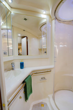 Sleek cream-toned yacht bathroom with curved glass shower, large mirror, built-in sink, blue soap dispenser and green towel, modern marine fixtures