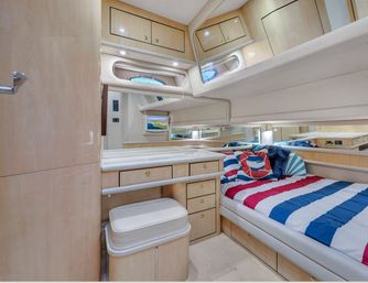 Cozy luxury yacht cabin interior with light wood finishes, nautical red-white-blue striped bedding, built-in drawers and cabinets, vanity with cushioned stool, porthole window and mirrored walls.