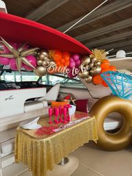 Bachelorette party setup aboard a yacht with gold, pink and orange balloon garland, Bride to be banner, giant gold ring float, sequin gold tablecloth and hot-pink champagne flutes