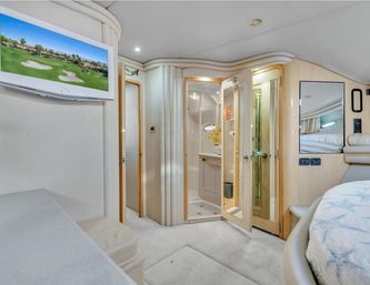 Luxury yacht cabin interior with cream wood finishes, round bed with patterned bedding, wall-mounted flat-screen TV, open glass-doored ensuite bathroom, mirrored accents and plush carpet