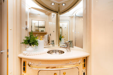 Cream-toned yacht bathroom vanity with round stainless sink, chrome faucet, mirrored corner cabinets, white soap dispensers and a small green plant.