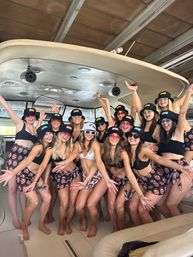 Cheerful group of women in matching bikinis, bucket hats and face-print sarongs posing on a motorboat under a covered marina