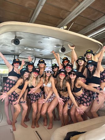 Cheerful group of women in matching bikinis, bucket hats and face-print sarongs posing on a motorboat under a covered marina
