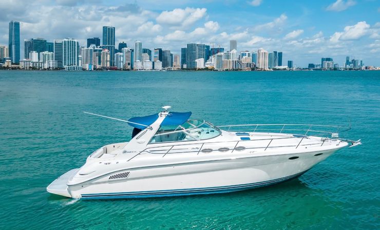 White luxury motor yacht gliding on turquoise water with the Miami skyline of high-rise buildings under a bright blue, partly cloudy sky
