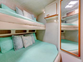 Compact yacht cabin with seafoam-green bunk beds, decorative starfish pillow, mirrored wall, overhead hatch and built-in storage