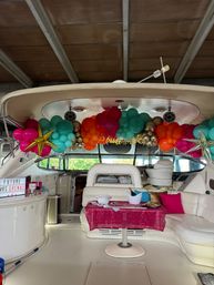 Vibrant balloon garland with gold star balloons decorates a luxury yacht interior for a bachelorette celebration, pink sequin tablecloth, champagne bucket and white leather seating