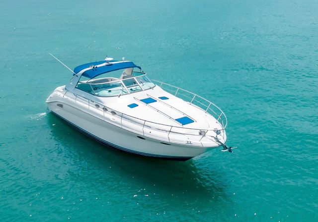 Aerial view of a sleek white motor yacht with blue canopy floating on calm turquoise tropical water, summer boating scene.