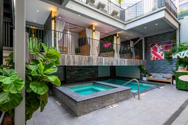 Modern downtown boutique hotel courtyard with tiled hot tub and plunge pool, upper-level curtained cabanas, tropical potted plants and cozy lounge seating