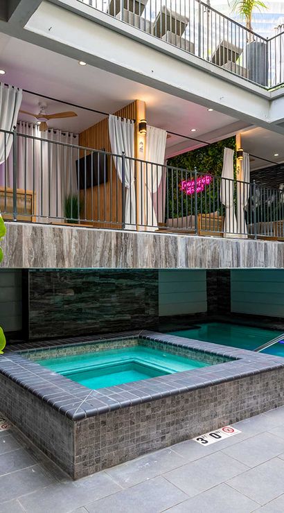 Modern downtown boutique hotel courtyard with tiled hot tub and plunge pool, upper-level curtained cabanas, tropical potted plants and cozy lounge seating