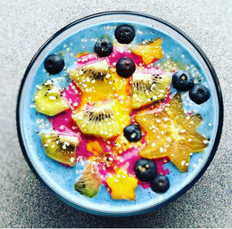 Vibrant blue spirulina smoothie bowl topped with kiwi, starfruit, blueberries, mango and pink dragonfruit swirl, sprinkled seeds — tropical healthy breakfast bowl