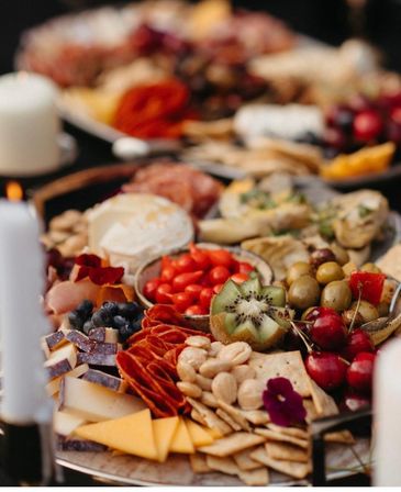 Vibrant charcuterie board with assorted cheeses, sliced cheddar, cured meats, crackers, mixed nuts, olives, cherries, kiwi and berries on a styled party platter.