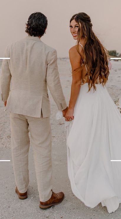 Bride in flowing white gown and groom in a light linen suit holding hands as they walk along a sandy beach shoreline at sunset with ocean waves and a faux video REC overlay