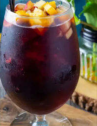Refreshing chilled red sangria in a stemmed glass topped with diced peaches on a wooden table